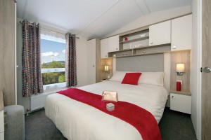 a double bed in a static caravan, made up with white and red bedding